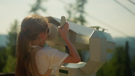 una chica curiosa explora el impresionante paisaje natural de la región montañosa a través de binoculares en un lugar turístico muy visitado en las vacaciones de verano. memoria de la infancia en cámara lenta