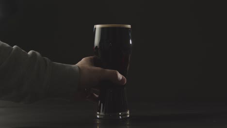 persona recogiendo una pinta de cerveza negra irlandesa en vidrio contra el fondo negro del estudio para celebrar el día de san patricio