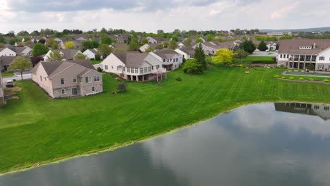 Aerial-flyover-lake-with-fountain-in-front-of-single-family-homes-during-sunny-day