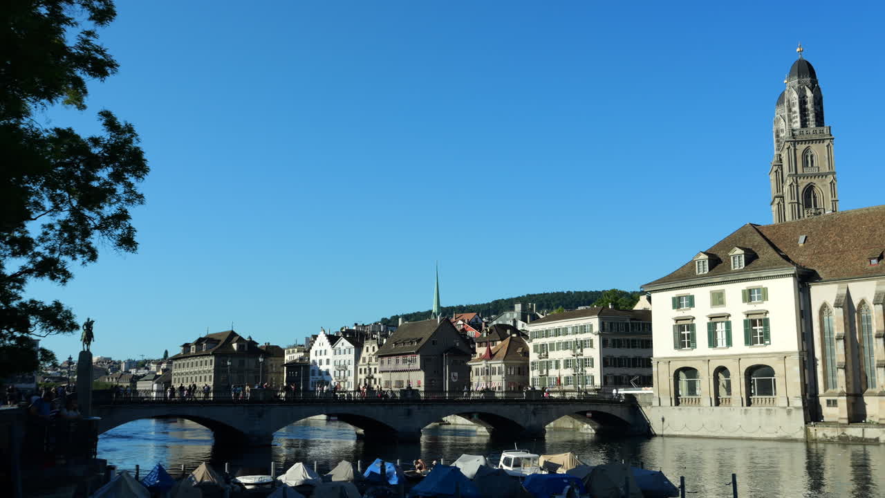 View of Zurich with people walking over bridge. Towers of Grossmünster on right. Static