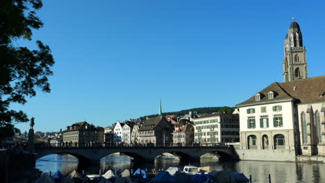 view of zurich with people walking over bridge. towers of grossmünster on right. static