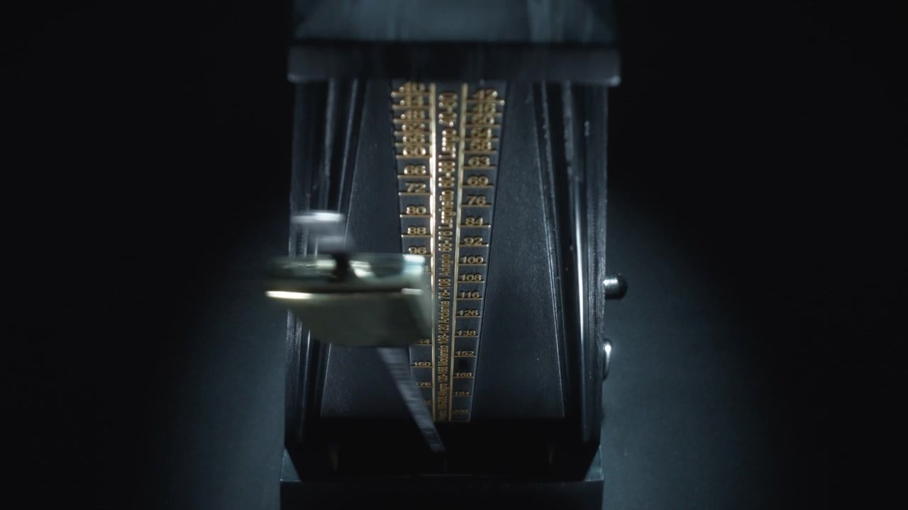 Abstract dolly shot of an old-fashioned black metronome swinging back and forth