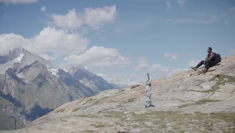 black male climber with backpack wiping sweat and resting in thought on mountainsde near the matterhorn in switzerland