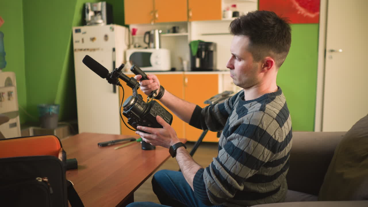 Man reaching for microphone in camera equipment bag, studio environment with wooden table. Camera gear, lenses, and other equipment neatly organized. Bright green walls create a cozy atmosphere
