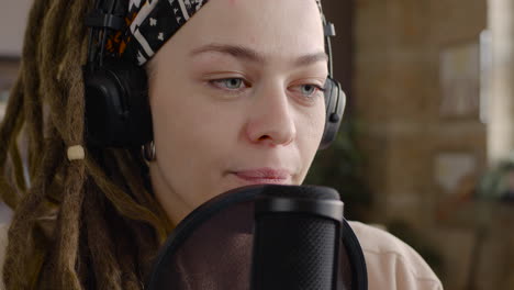 close up view of woman with dreadlocks recording a podcast talking into a microphone sitting at desk