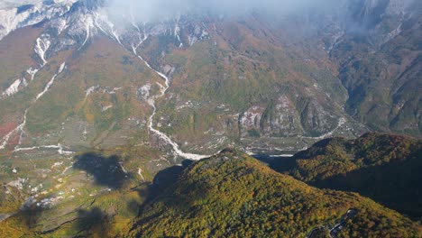 flying across the clouds over a beautiful valley covered in colorful foliage of autumn, in the alps of albania