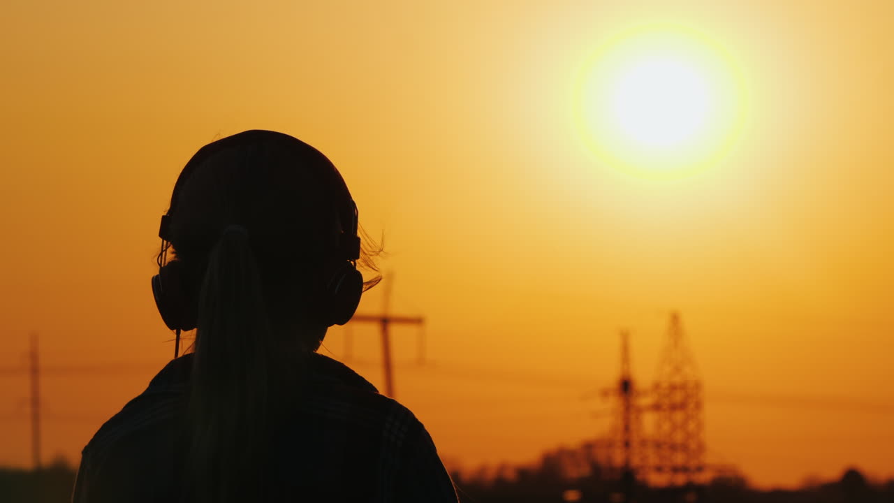 силуэт девушки в наушниках, слушающей музыку на фоне большого заходящего солнца ан