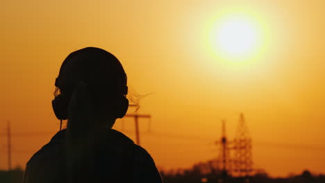silueta de una chica con auriculares escuchando música con el telón de fondo de una gran puesta de sol y