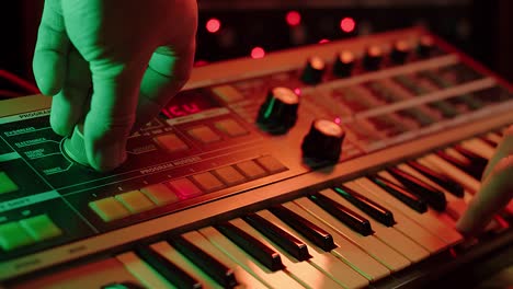 slow-motion shot van een man die toetsen speelt en aan knoppen draait op een vintage synth, rode en groene stemming