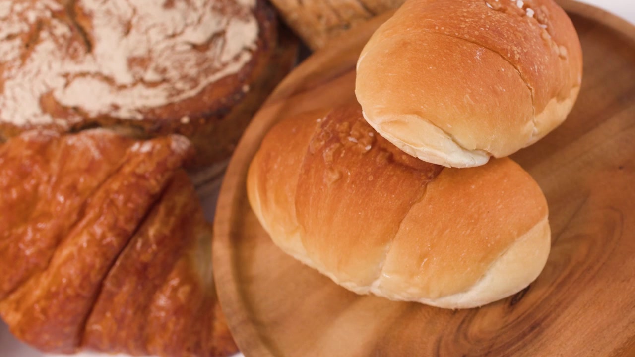 Close-up rotating view of sourdough, croissants, and rolls on a rustic wooden plate.