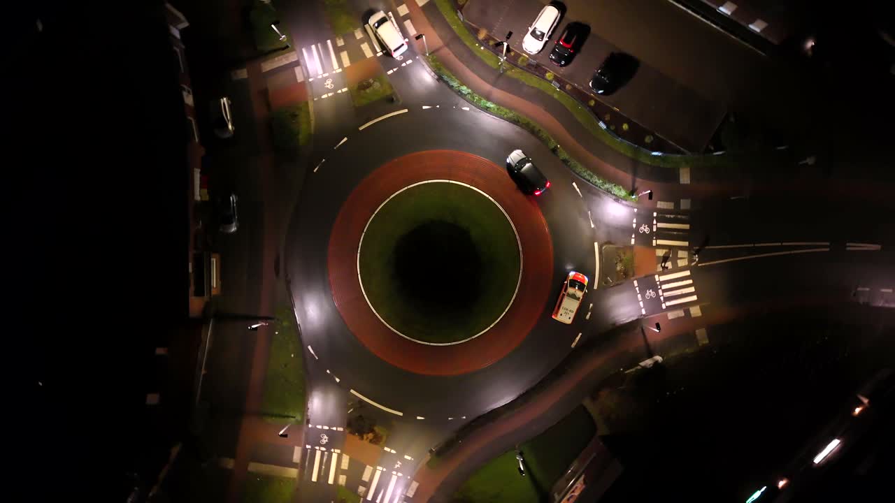 Cars in roundabout during night. Warm lighting streetlights in american town. Aerial top down. Rising circling shot.