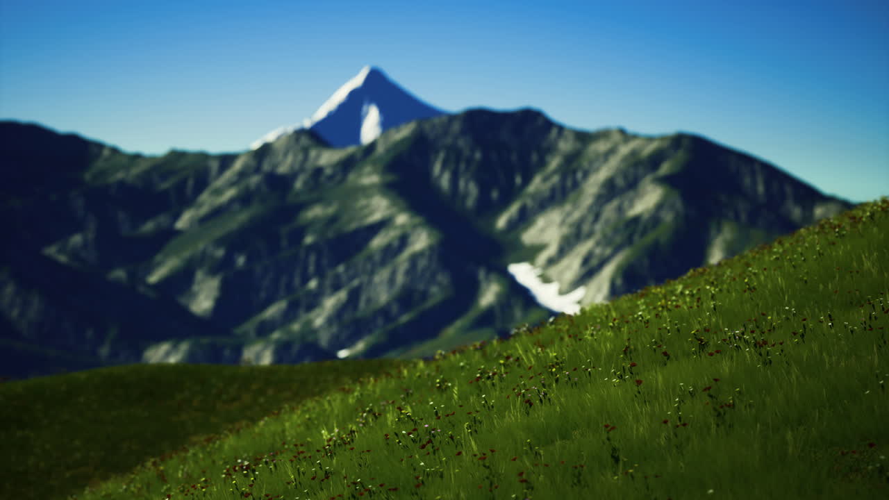 Majestic mountain peak rises above vibrant green meadow in clear sky