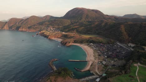 paisaje aéreo de drones de la bahía japonesa del mar azul en kyoto, costa de verano de la isla de kyotango, playa de arena blanca con un pueblo cercano, japón durante el día, fondo de la cordillera