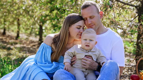 woman in blue dress kisses her lovely son on the head, while her husband kisses her on the forehead. loving family of three in the nature in spring.