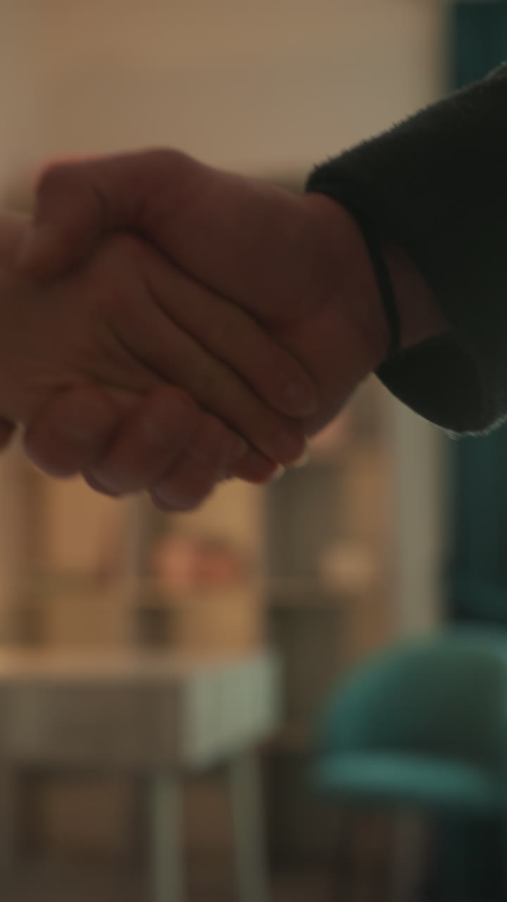 stretta di mano in clinica tra professionista e paziente durante una consultazione per massaggio a microcorrente, primo piano delle mani con presa delicata, illuminazione calda di una lampada e sedia color ottanio in sfondo sfocato, accogliente