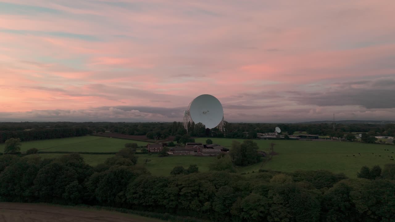 Large satellite dish at the Jodrell Bank Observatory under a pink sky
