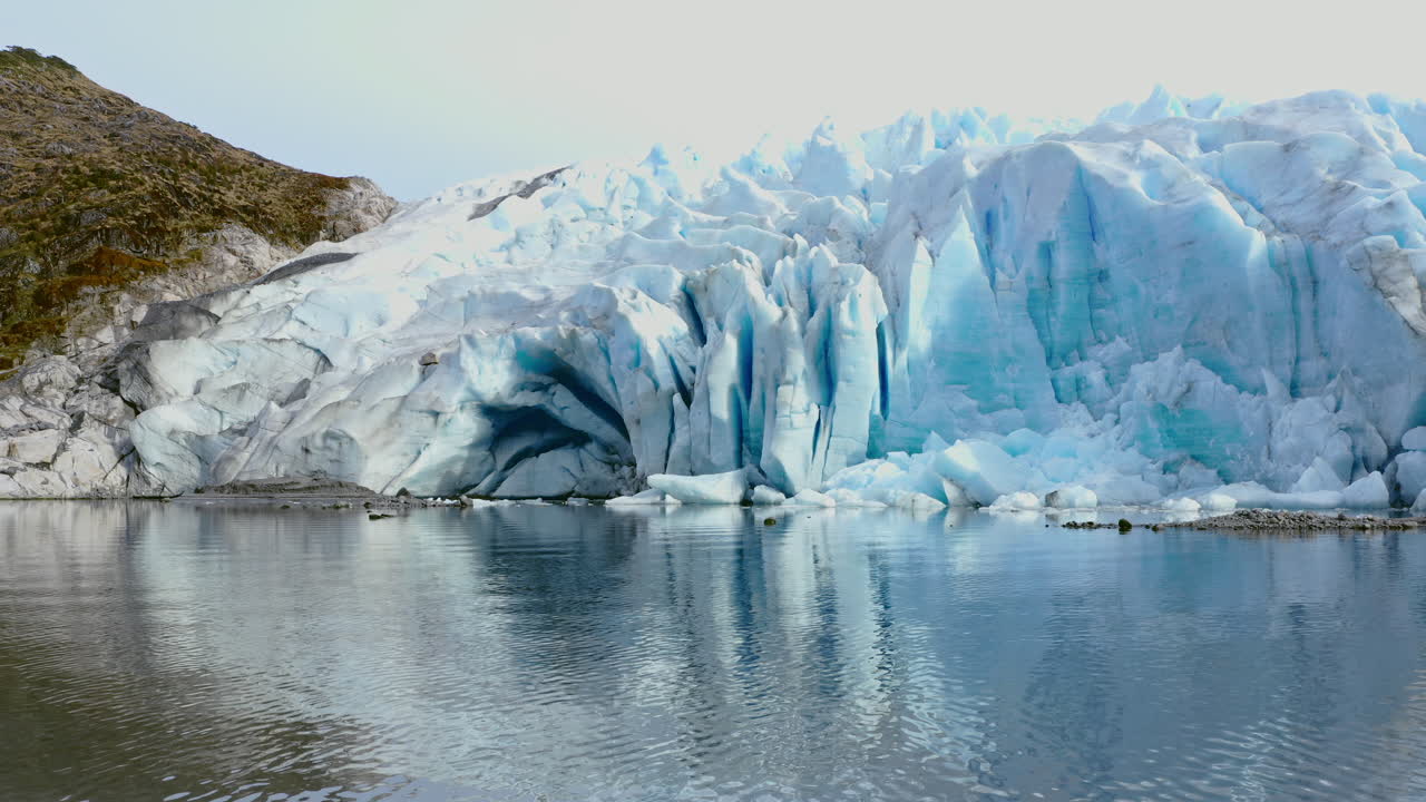 Icebergs cluster in Beagle Channel near glacier front under cloudy skies and arctic wind, low approach