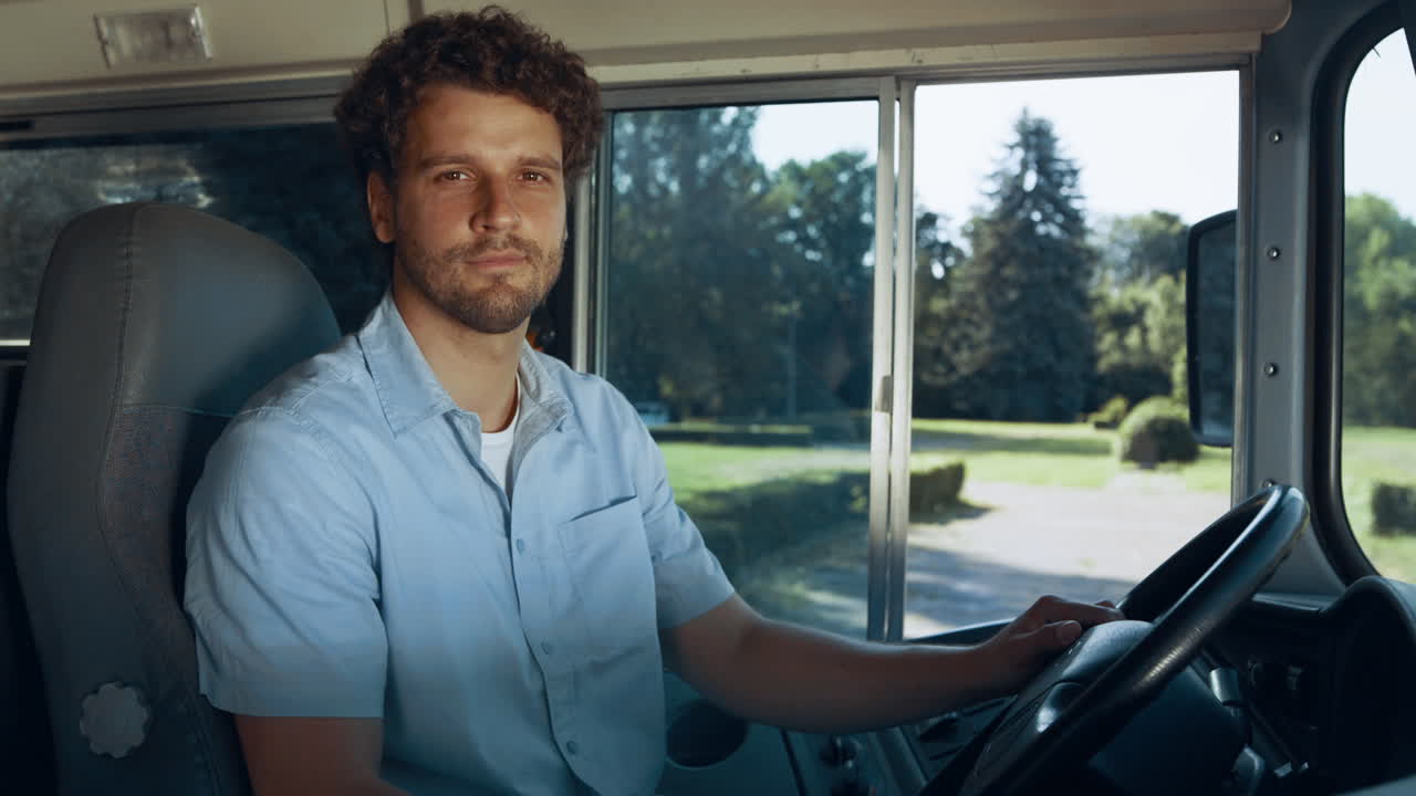 School bus driver sitting cabin close up. Man hold steering wheel look in camera