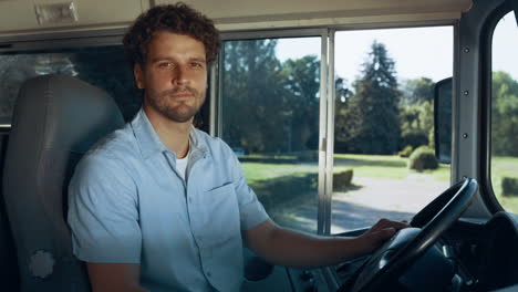 School-bus-driver-sitting-cabin-close-up.-Man-hold-steering-wheel-look-in-camera