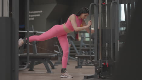 A-young-woman-lifts-her-leg-in-a-crossover-to-train-her-thigh-and-leg-muscles.-Buttocks-training.-A-professional-female-athlete-does-leg-exercises