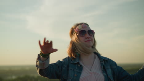 a joyful woman wearing a floral headband and sunglasses is seen dancing in an open field