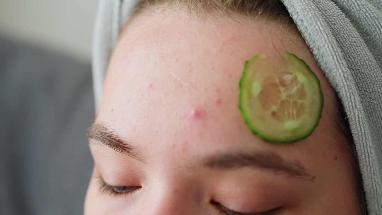 Close-up view of lady placing a cucumber slice on her forehead while relaxing, she's practicing self-care and enjoying a spa-like experience at home in a calm and peaceful environment