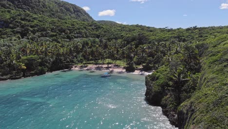 Aerial-backwards-shot-of-Playa-Madama-with-bay-surrounded-by-Beautiful-green-hills-in-SAMANA-LAS-GALERAS,-Dominican-Republic---Tropical-spot-with-palm-trees-and-sandy-beach