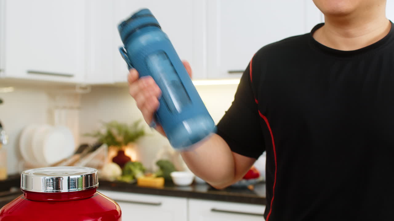 Man shaking shaker bottle in kitchen mixing sports supplement drink electrolyte creatine protein gym