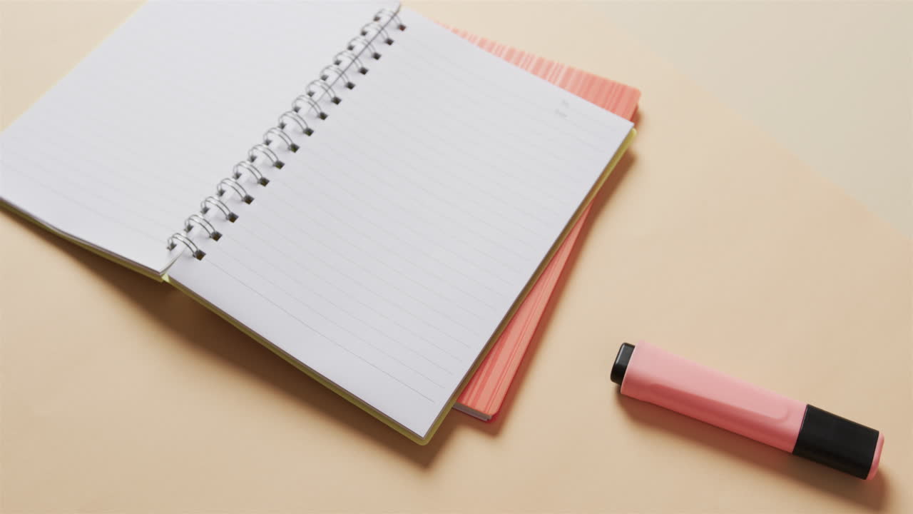Close up of open notebook with pink marker on beige background, in slow motion