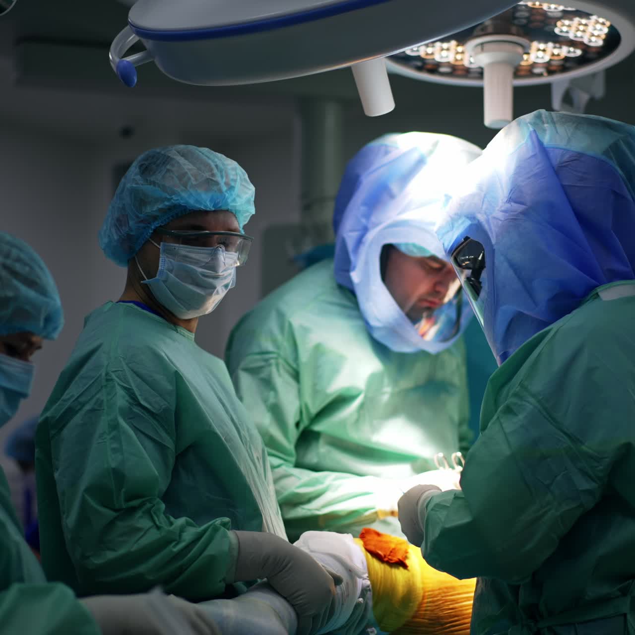 Professional team of surgeons wearing protective suits and helmets stand around operational table. Doctors perform arthroscopy on a leg