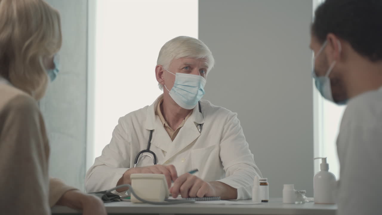 A Grey Haired, Middle Aged Doctor In A Facemask Asking Questions To A Young Black Man 1