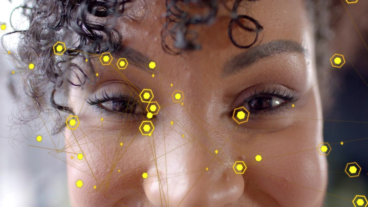 Vertical video: Adult woman smiling while yellow hexagons appearing and tracking face for tech demo