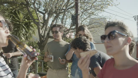 carefree friends talking together while eating pizza and drinking beer during a rooftop party