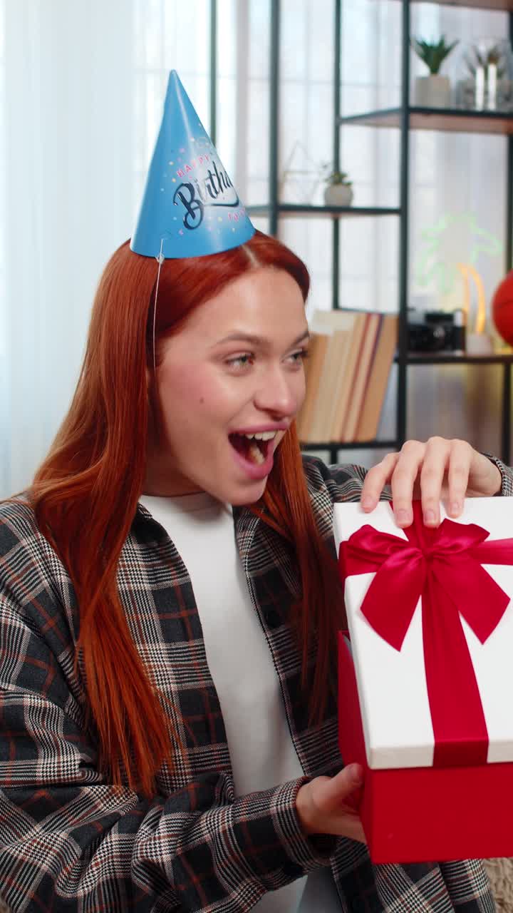 Mujer con sombrero de fiesta abriendo regalo de cumpleaños mirando agradablemente sorprendido y emocionalmente feliz
