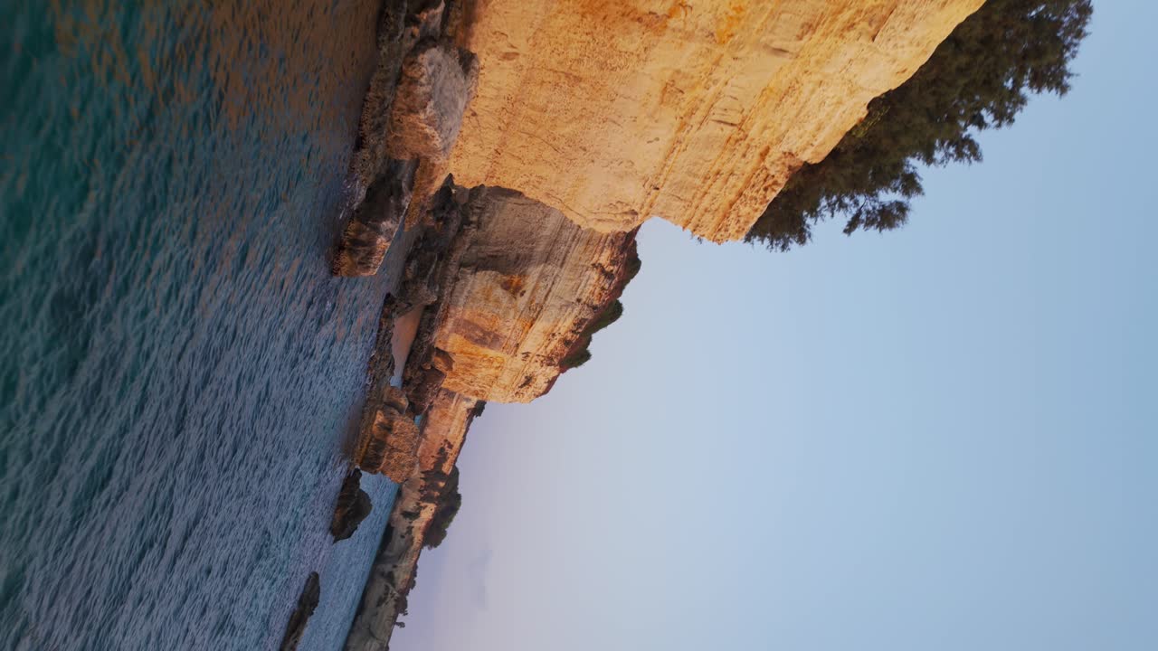 Dramatic drone movement pass along the golden limestone cliffs of Torre Sant’Andrea, Apulia, with turquoise Adriatic waves, sea stacks, and a dynamic roll movement at sunset