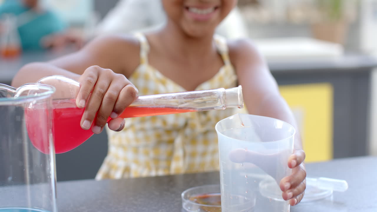 In a school classroom setting, a young biracial girl conducts a science experiment