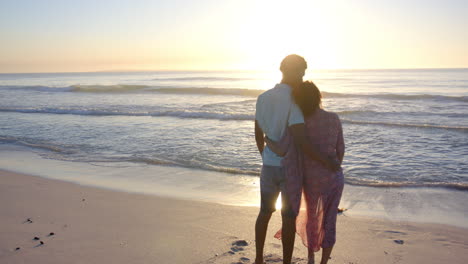 biracial couple embraces, silhouetted against a beach sunset with copy space