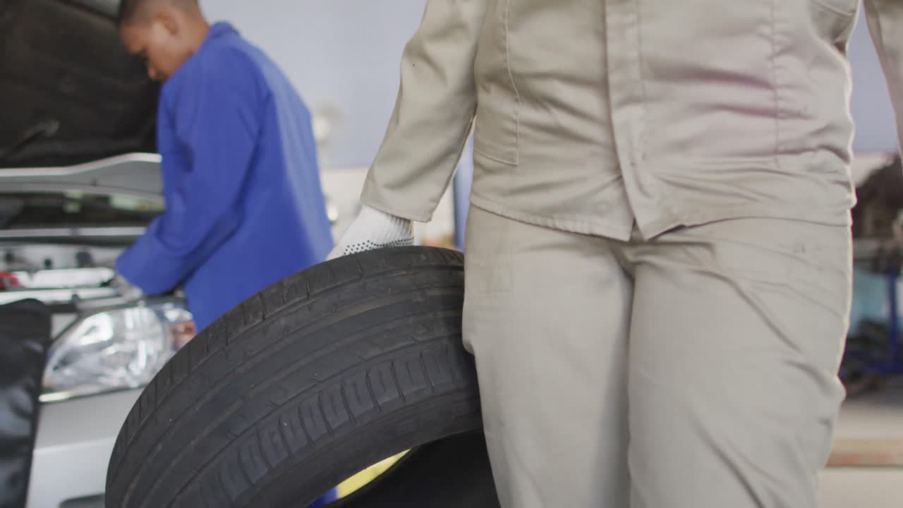 Video of midsection of biracial female car mechanic holding tyre