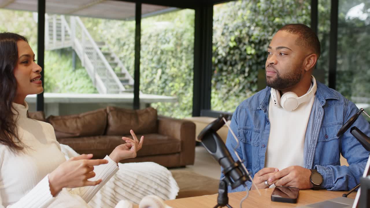 Kvinde læner sig frem og optager stuepodcast med afroamerikansk mand ved hjælp af mikrofon-smartphone.