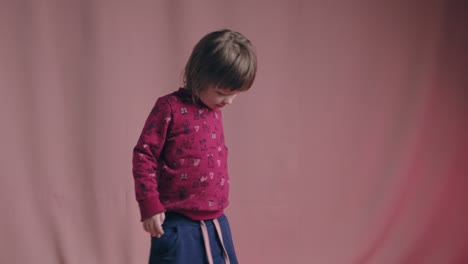 funny little boy is dancing, rejoicing and making funny faces. pink background