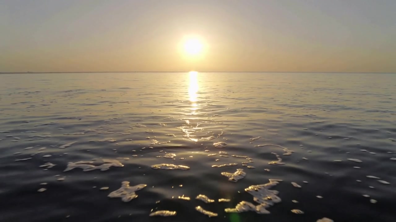 Bobbing camera capturing sea surface and sun reflection on water at sunrise, foam drifting