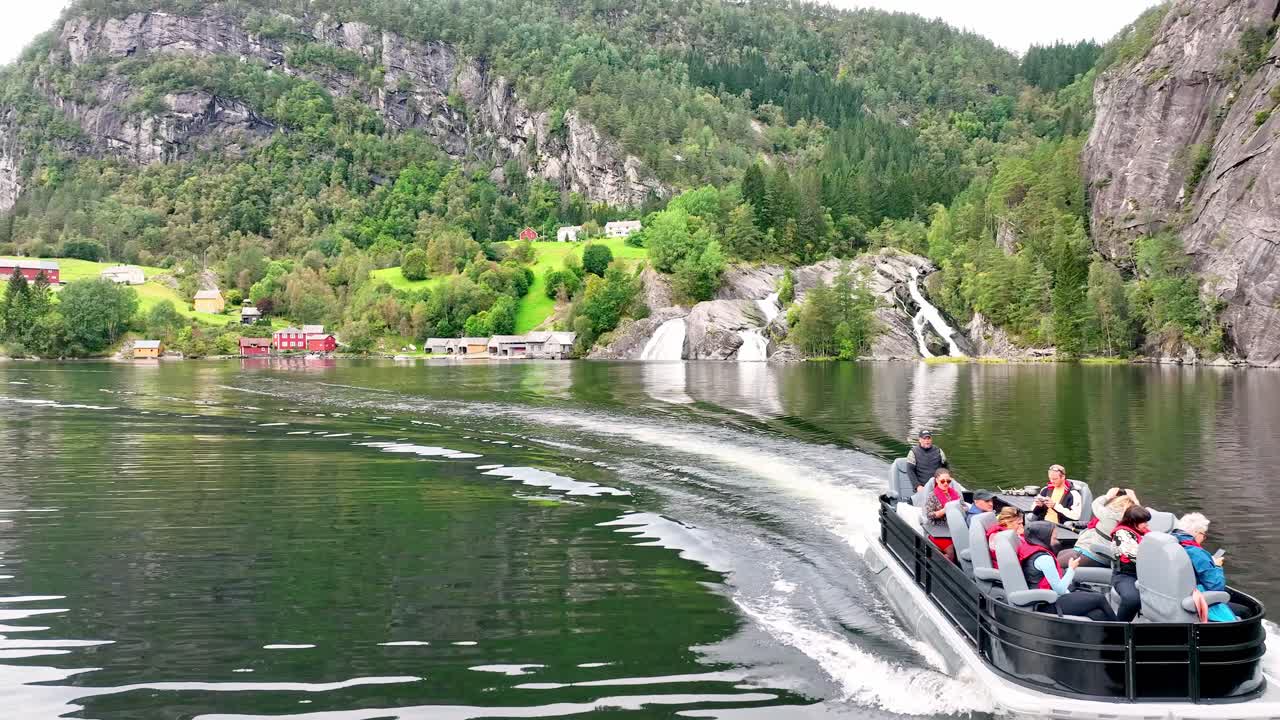 Pontoon boat passes closely under a slow motion drone shot with Tysseknappen waterfalls in the background