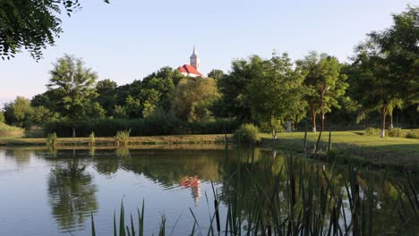 Ondas-En-Un-Pintoresco-Estanque-En-Los-Jardines-Del-Evento,-Reflejando-El-Campanario-De-La-Iglesia-Y-Los-árboles-En-La-Orilla.