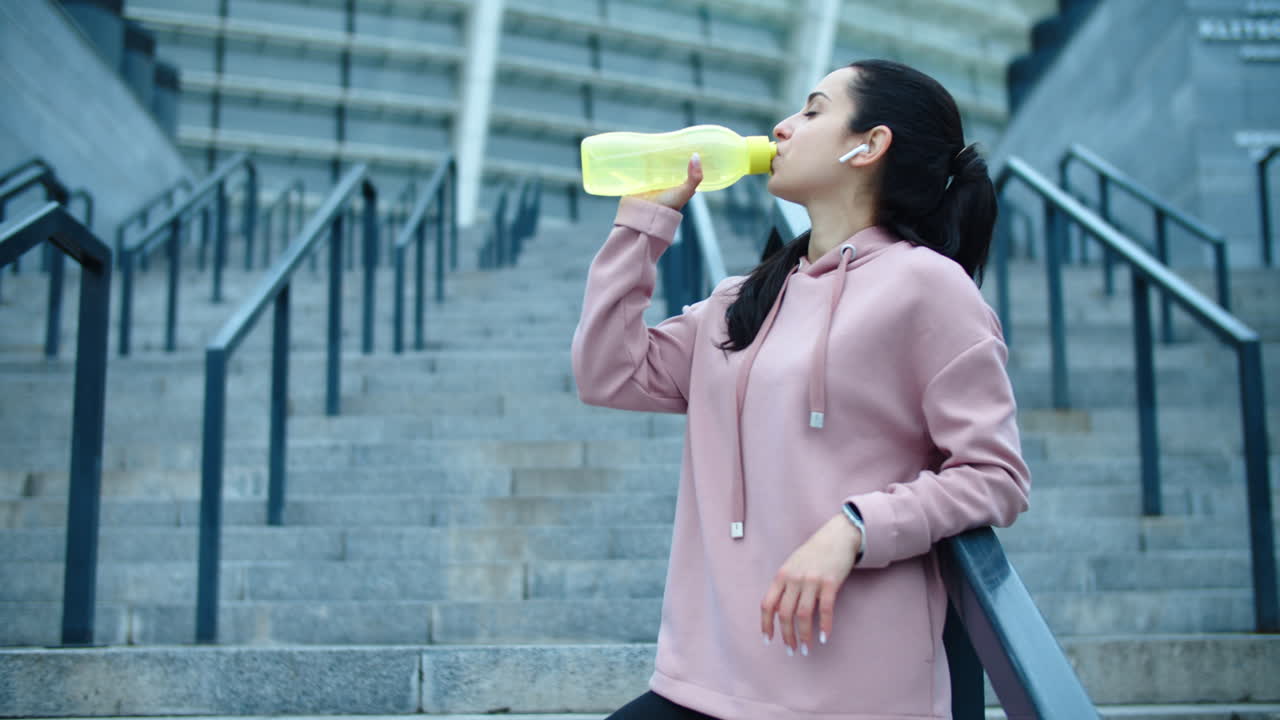 mujer atleta bebiendo agua a cámara lenta. mujer sedienta relajándose en la escalera