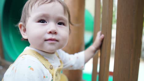 niña de raza mixta sosteniendo una cerca de madera del patio de recreo mira y sonríe a la cámara