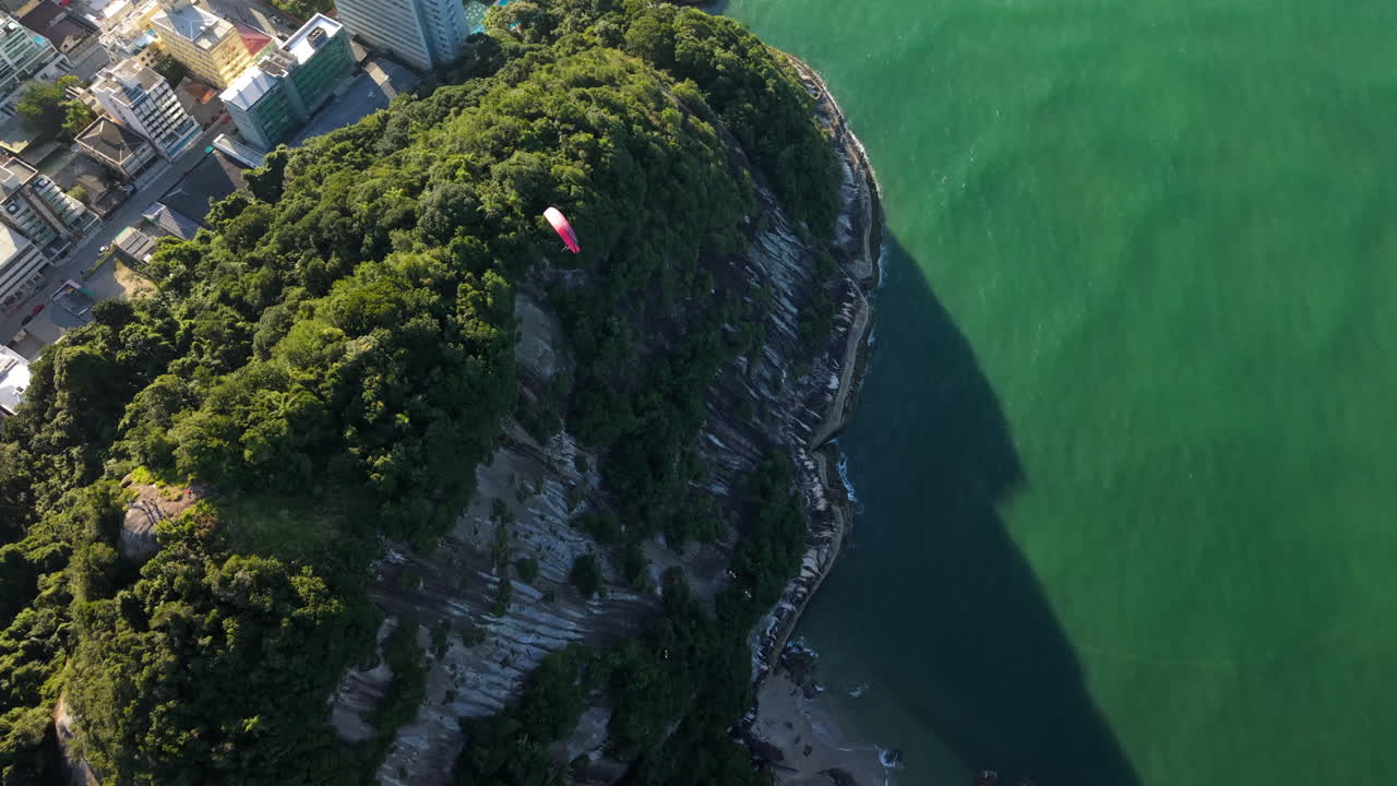 Paraglider flying high over Morro do Boi, revealing Caioba's urban landscape and sweeping Atlantic Ocean coastline in Parana, Brazil