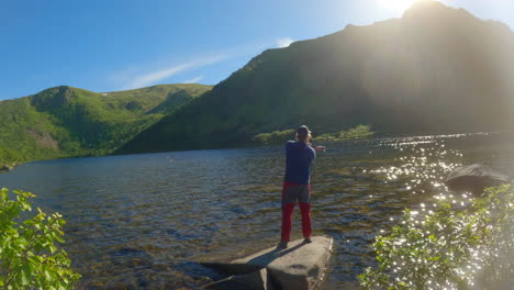 Hombre-Usando-Caña-De-Pescar-En-Un-Lago-De-Montaña-En-Un-Agradable-Día-Soleado,-Tiro-Estático-Con-Destello-De-Lente