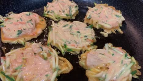 korean kimchi-veggie pancakes frying on a large skillet with oil bubbling underneath