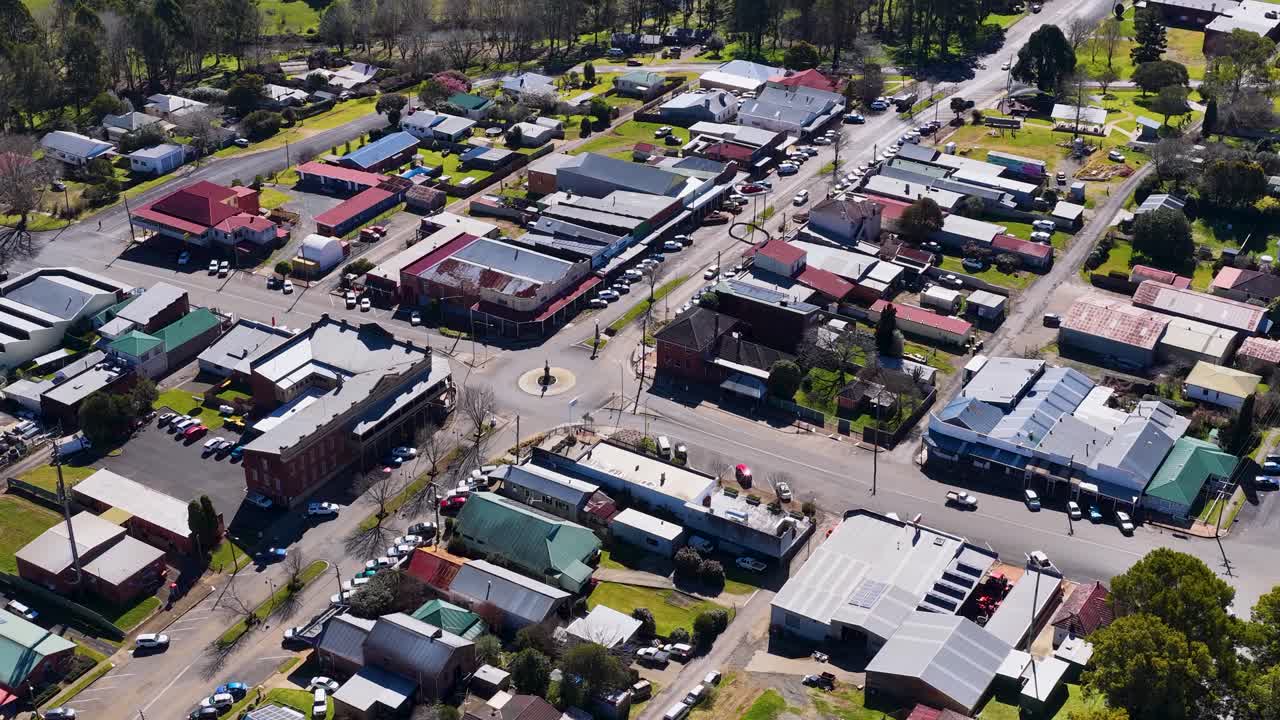 Drone ascends above Dorrigo town, revealing streets, shops, cars, and rural surroundings in daylight