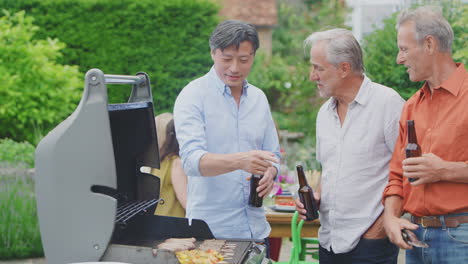 three senior male friends cooking outdoor barbeque and drinking beer at home together